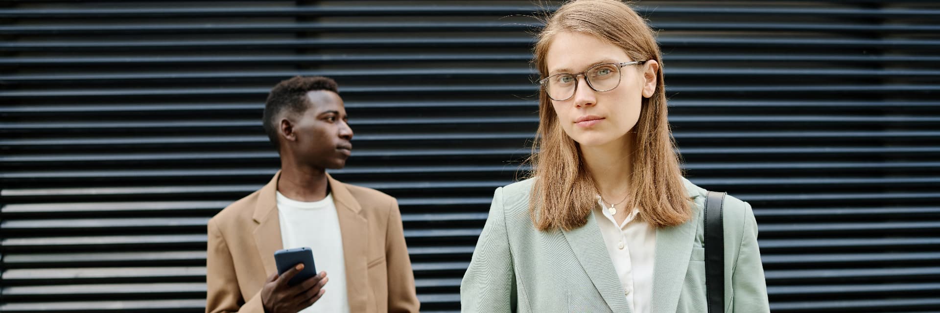 Two young professionals outdoors, one looking directly ahead
